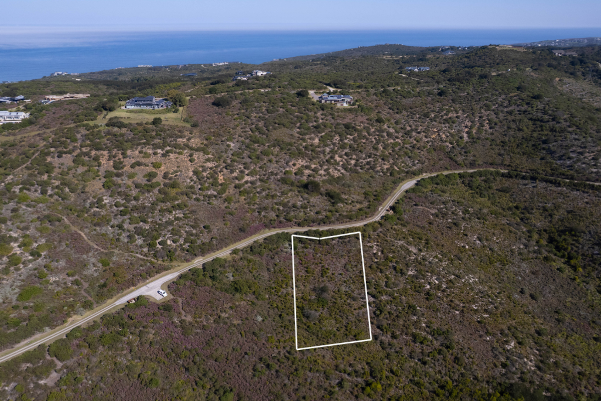 Aerial view of a vacant residential plot situated in a coastal landscape with surrounding natural vegetation and nearby road access.