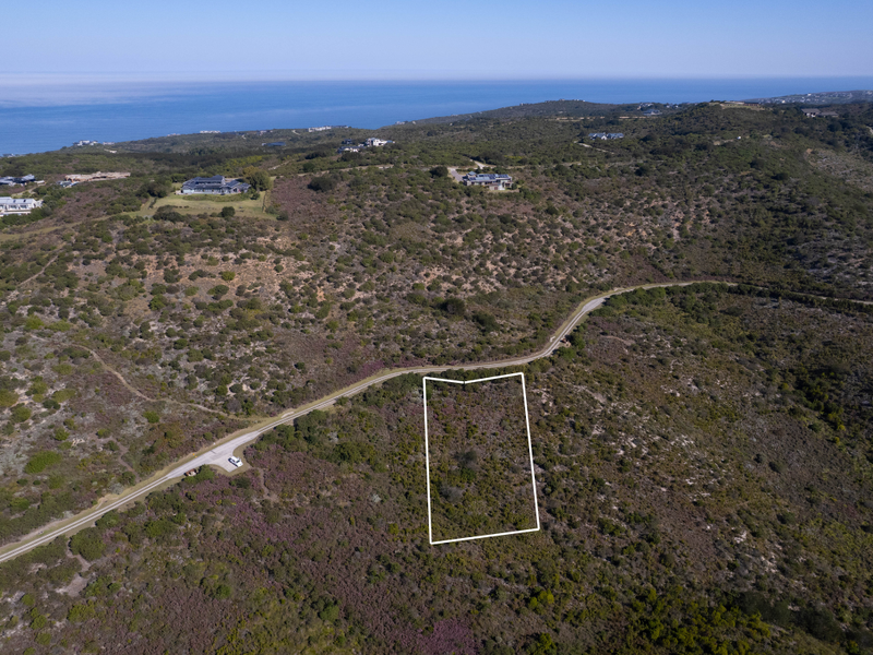 Aerial view of a vacant residential plot situated in a coastal landscape with surrounding natural vegetation and nearby road access.