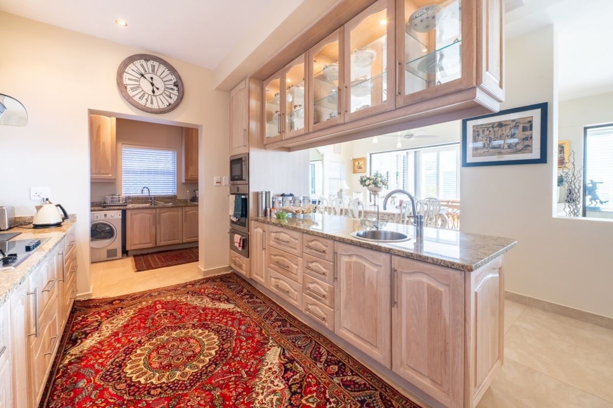 A well-appointed kitchen featuring light wood cabinetry, granite countertops, built-in appliances, and a convenient adjacent scullery area.