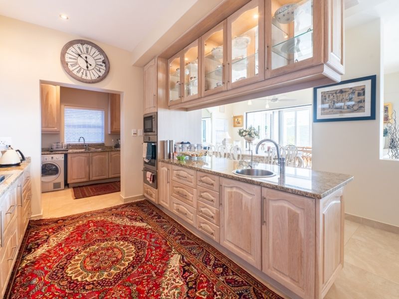 A well-appointed kitchen featuring light wood cabinetry, granite countertops, built-in appliances, and a convenient adjacent scullery area.