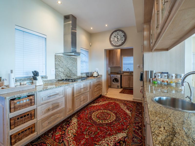 A well-maintained kitchen featuring granite countertops, wooden cabinetry, a stainless steel extractor fan, and a built-in gas hob, with an adjacent scullery area.