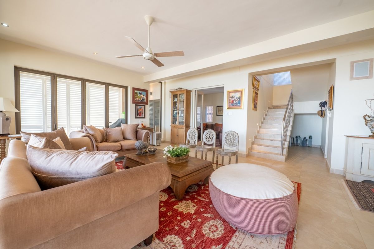 Spacious living room featuring tiled flooring, a ceiling fan, and an open staircase with a modern metal railing leading to the upper level.
