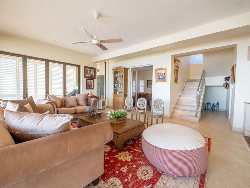 Spacious living room featuring tiled flooring, a ceiling fan, and an open staircase with a modern metal railing leading to the upper level.