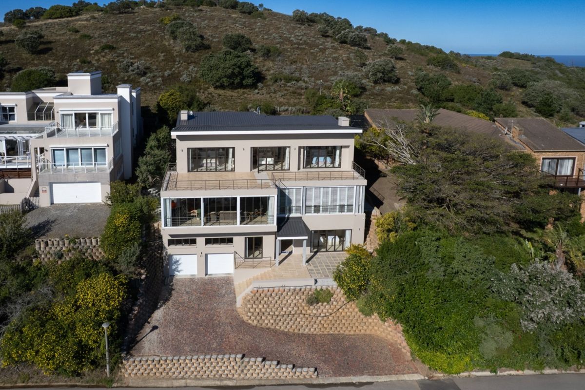 Aerial view of a multi-level residential property featuring a double garage, paved driveway, retaining walls, and multiple balconies set against a hillside.