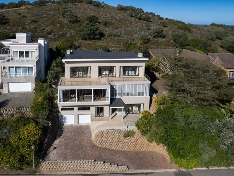 Aerial view of a multi-level residential property featuring a double garage, paved driveway, retaining walls, and multiple balconies set against a hillside.