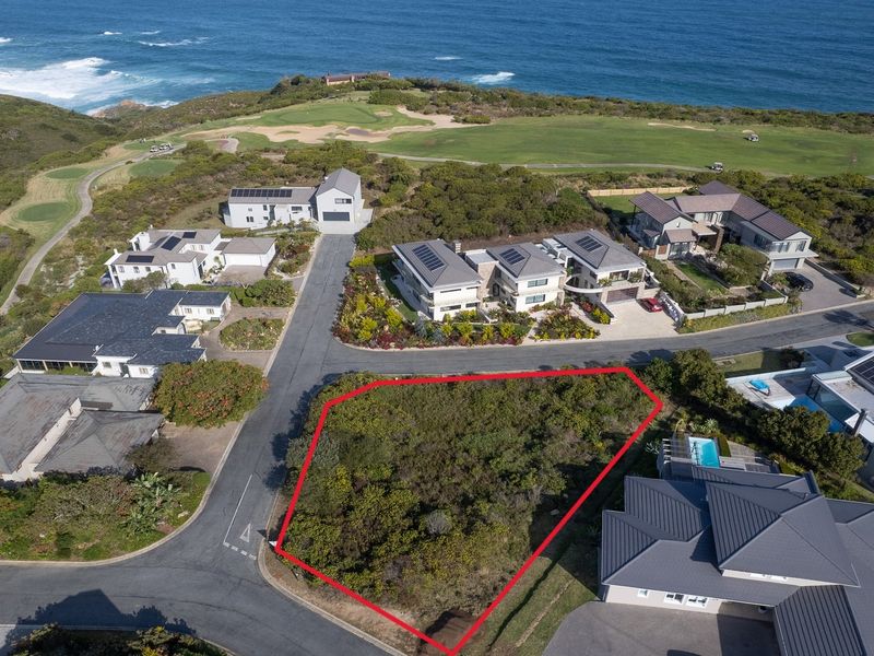An aerial view of a vacant residential plot situated in a coastal estate, featuring surrounding established homes and proximity to the ocean.