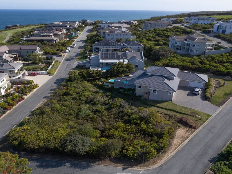 An aerial view of a vacant residential plot situated in a coastal estate, surrounded by established homes and paved road infrastructure.