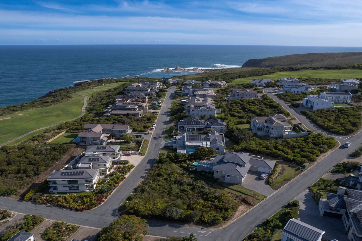 An aerial view of a coastal residential estate featuring modern homes, paved streets, and proximity to a golf course and the ocean.