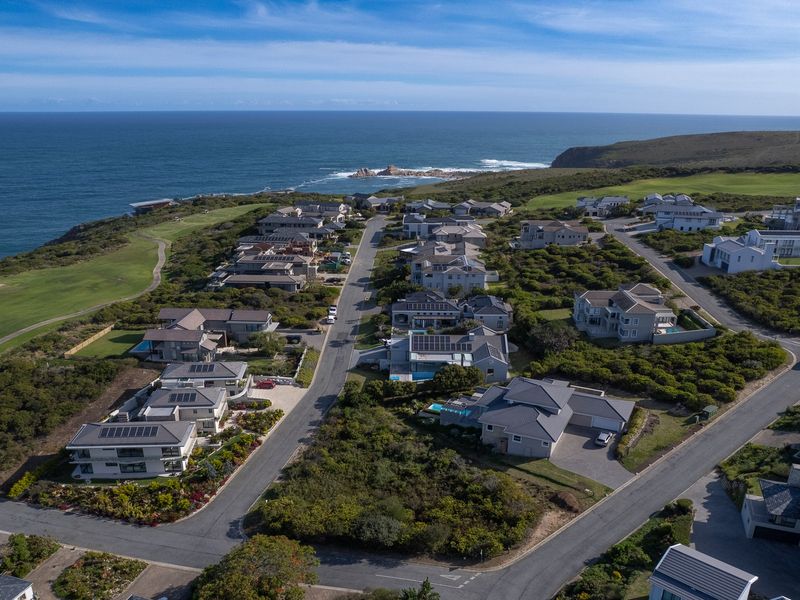 An aerial view of a coastal residential estate featuring modern homes, paved streets, and proximity to a golf course and the ocean.