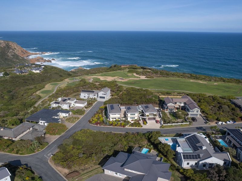Aerial view of a coastal residential estate featuring modern homes, paved streets, and proximity to a golf course and the ocean.