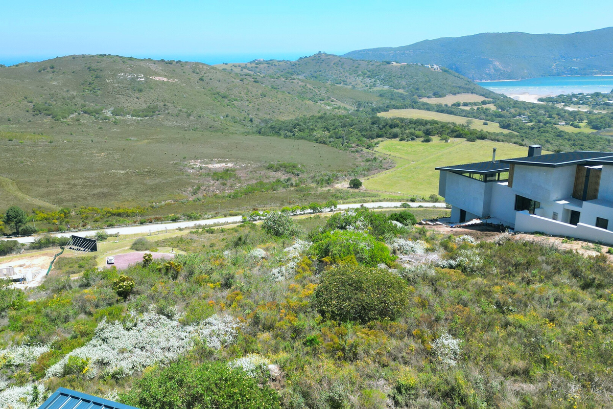 An elevated aerial view of a vacant residential plot featuring natural landscape, native vegetation, and proximity to an existing modern architectural home.