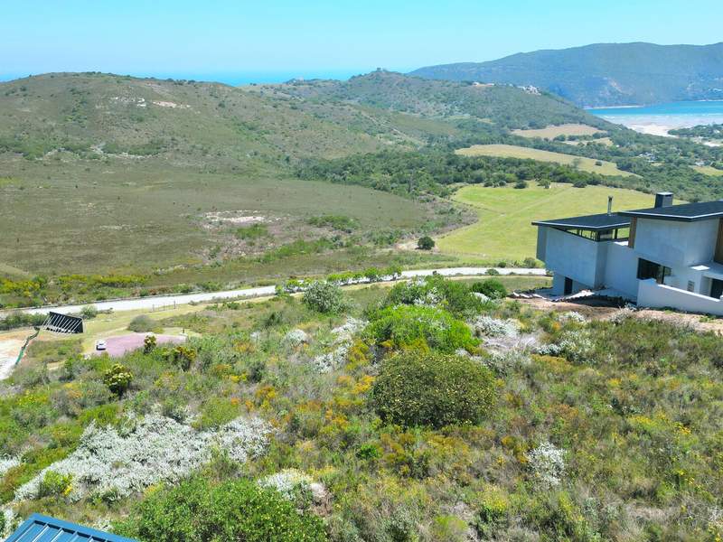 An elevated aerial view of a vacant residential plot featuring natural landscape, native vegetation, and proximity to an existing modern architectural home.