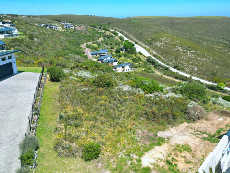 Aerial view of a vacant residential plot within a developed estate, featuring surrounding natural landscape and neighboring modern homes.