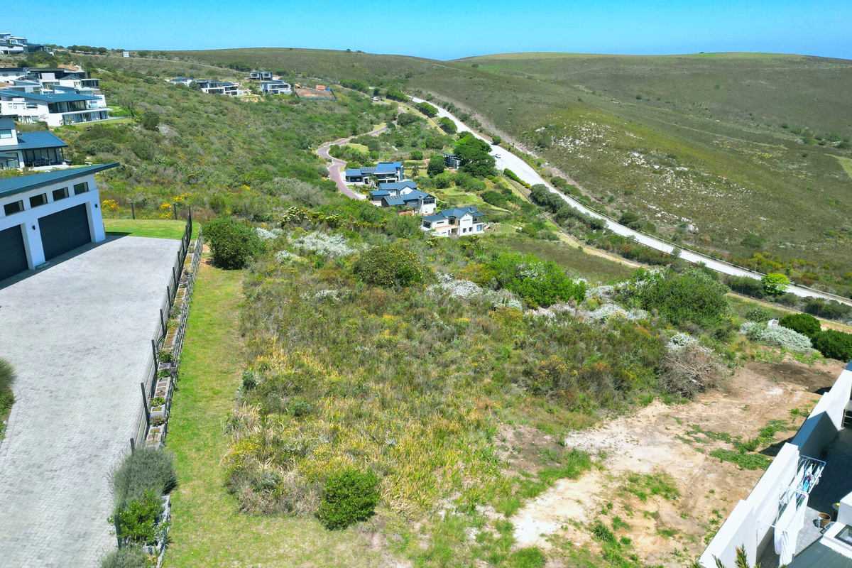 Aerial view of a vacant residential plot within a developed estate, featuring surrounding natural landscape and neighboring modern homes.