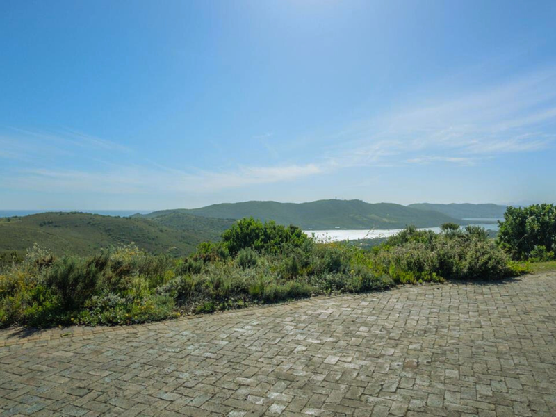 A scenic view overlooking rolling hills, natural vegetation, and a distant body of water from a paved residential driveway.