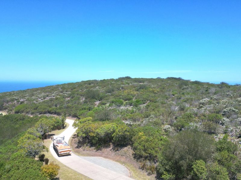 An aerial view of a vacant residential plot featuring natural coastal vegetation and a paved access road leading through the property.