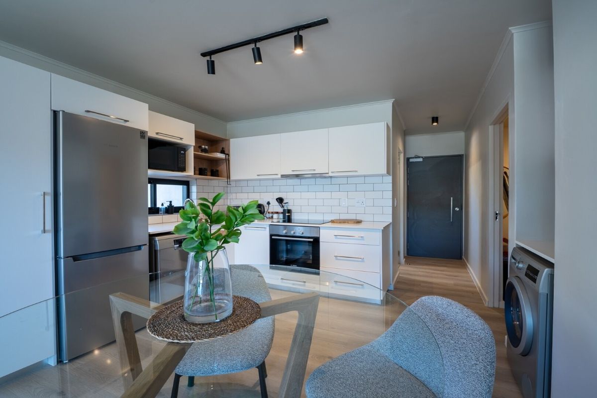 Modern open-plan kitchen featuring white cabinetry, subway tile backsplash, integrated appliances, and track lighting, seamlessly flowing into the living and dining area.