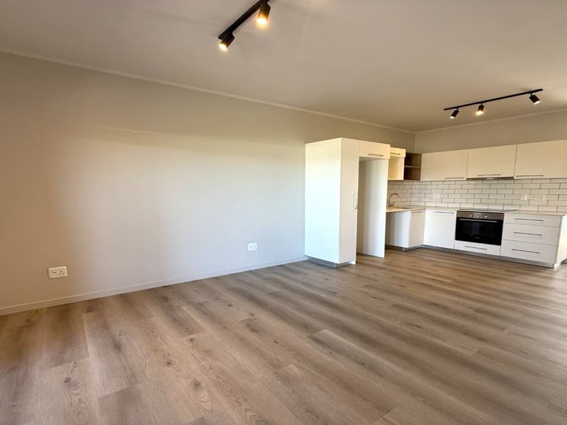 Modern open-plan living area featuring light wood-look laminate flooring, track lighting, and a contemporary kitchen with white cabinetry and subway tile backsplash.
