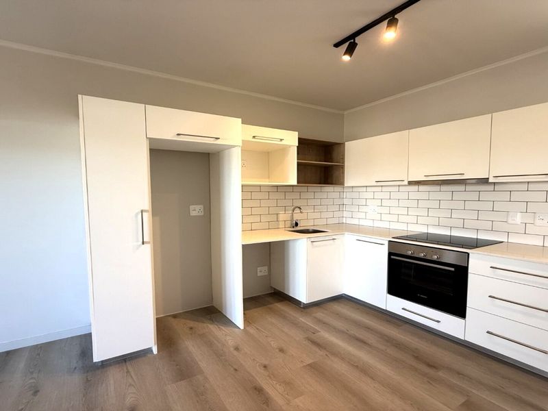 Modern kitchen featuring white cabinetry, subway tile backsplash, integrated oven and hob, and durable laminate flooring in a clean, contemporary layout.