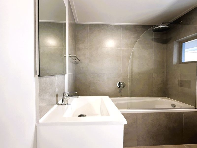 Modern bathroom featuring a vanity basin, tiled walls, and a bathtub with an integrated shower and glass screen.