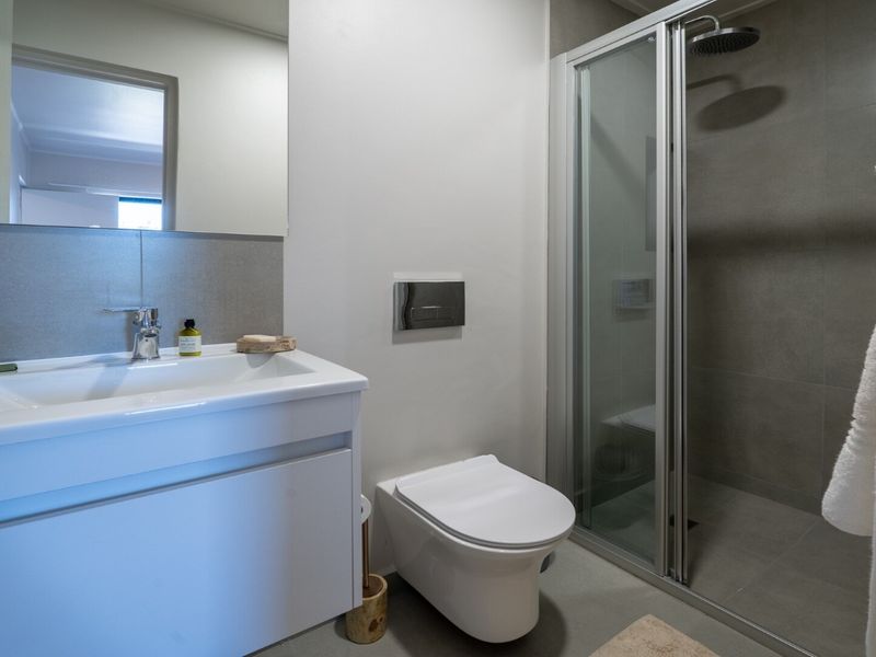 Modern bathroom featuring a wall-mounted vanity, wall-hung toilet with concealed cistern, and a walk-in shower with glass screen and neutral tiling.