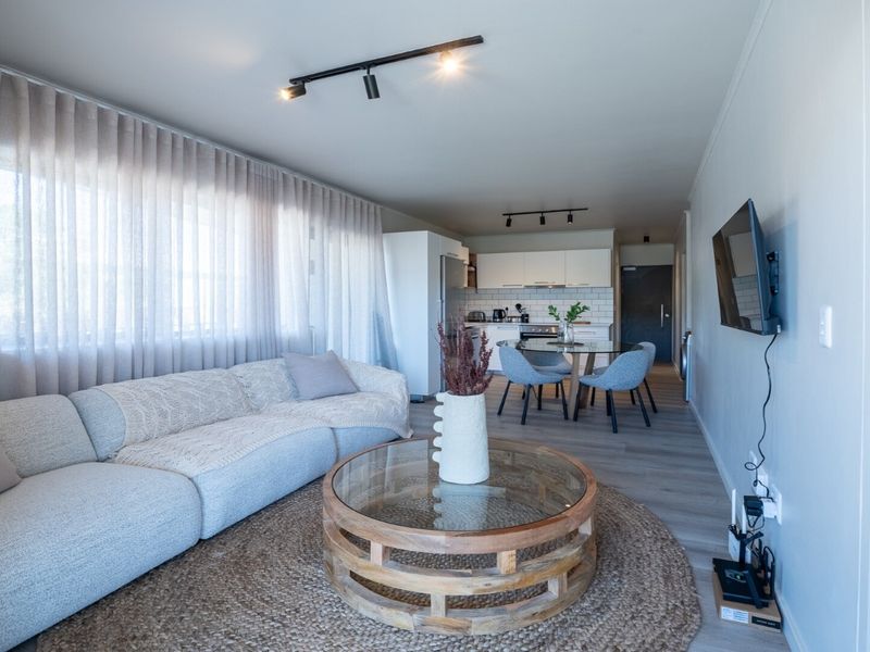 A bright open-plan living and dining area featuring modern track lighting, laminate flooring, and a well-appointed kitchen with subway tile backsplash.