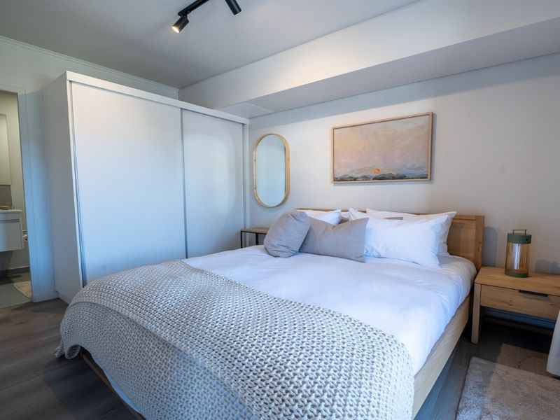 A well-maintained bedroom featuring modern track lighting, laminate flooring, and a built-in wardrobe, with convenient access to an adjoining en-suite bathroom.