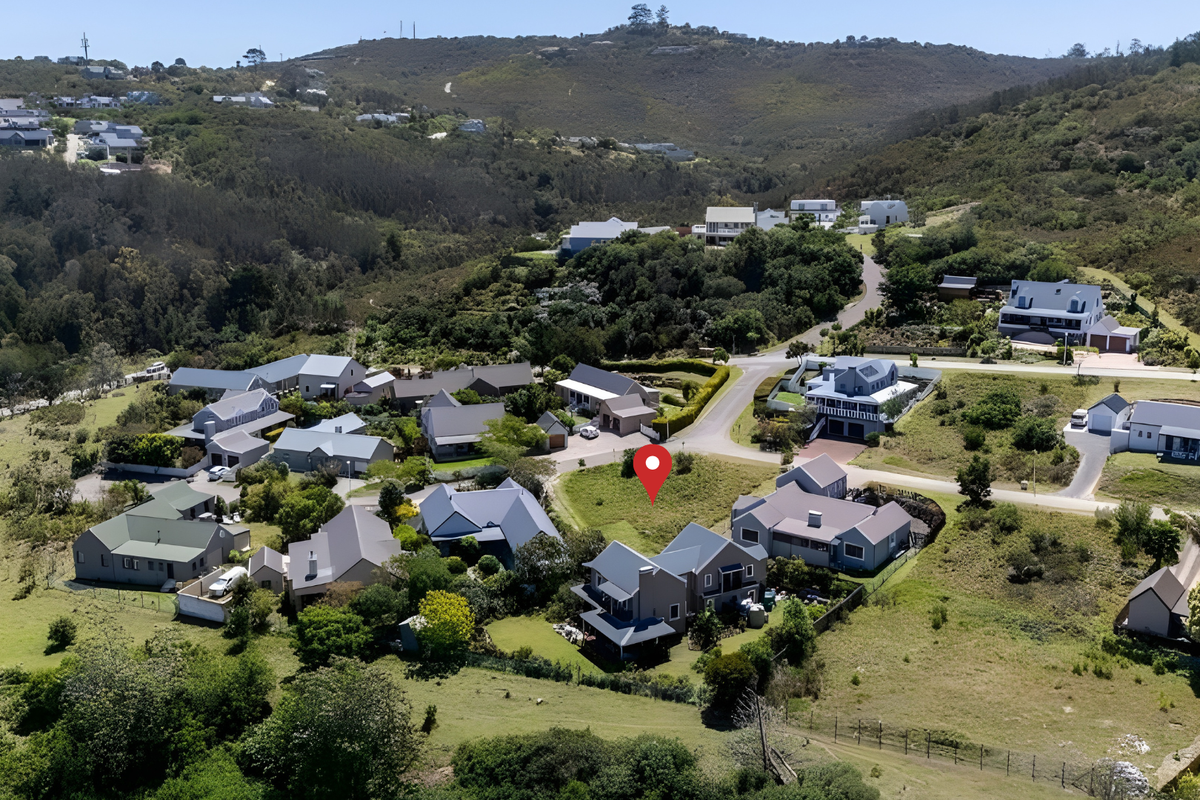 An aerial view of a vacant residential plot situated within a developed estate, surrounded by established homes and natural landscape.