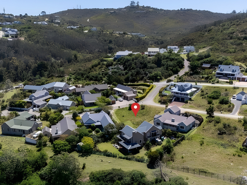 An aerial view of a vacant residential plot situated within a developed estate, surrounded by established homes and natural landscape.