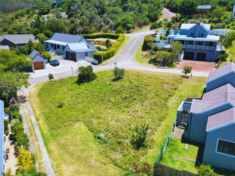 Aerial view of a vacant residential plot situated within a developed estate, featuring surrounding homes and established access roads.