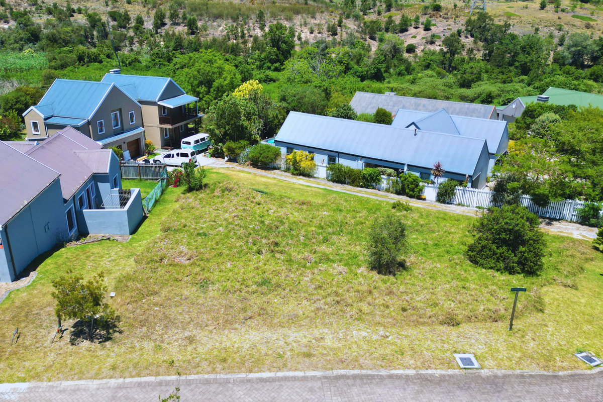 An aerial view of a vacant residential plot situated in a developed neighborhood with paved street access and adjacent homes.