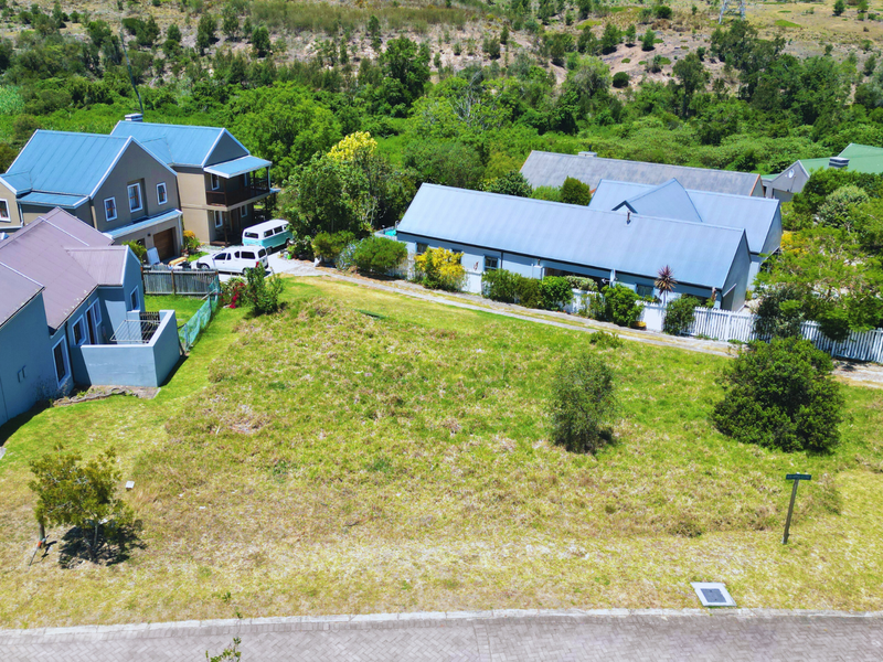 An aerial view of a vacant residential plot situated in a developed neighborhood with paved street access and adjacent homes.