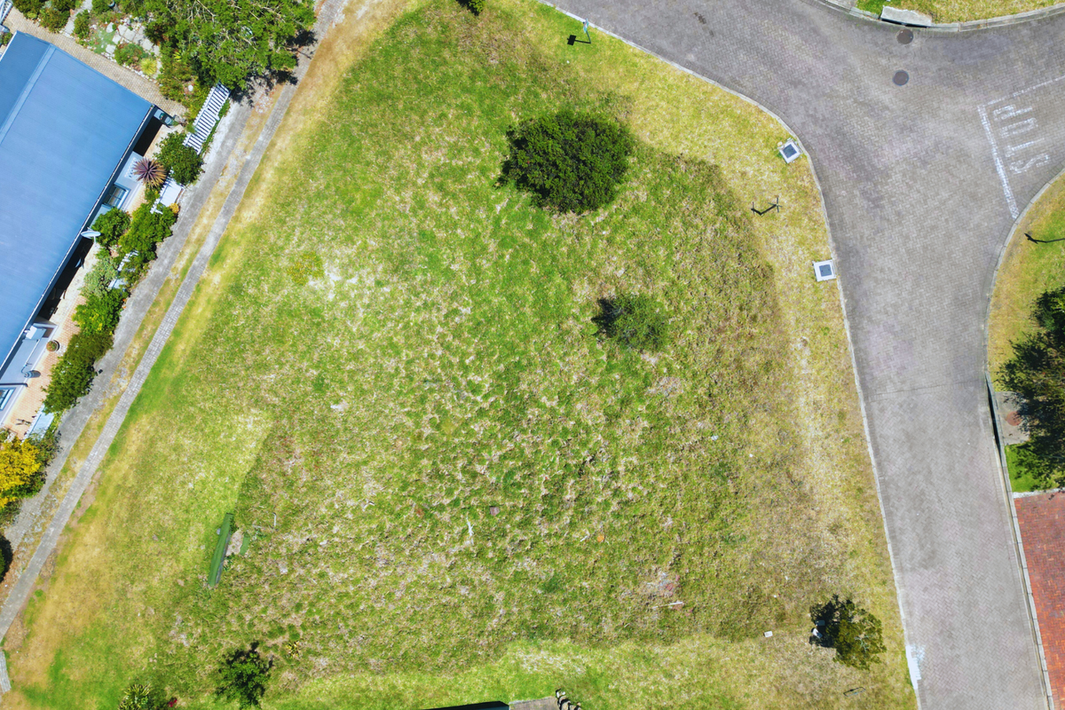An aerial view of a vacant residential plot situated on a corner lot, featuring established grass and proximity to paved street access.
