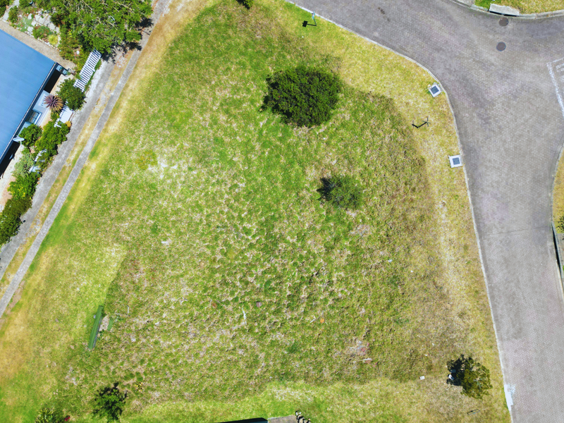 An aerial view of a vacant residential plot situated on a corner lot, featuring established grass and proximity to paved street access.