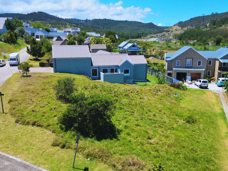 An elevated aerial view of a residential vacant land plot situated within a developed estate, featuring surrounding homes and paved street access.