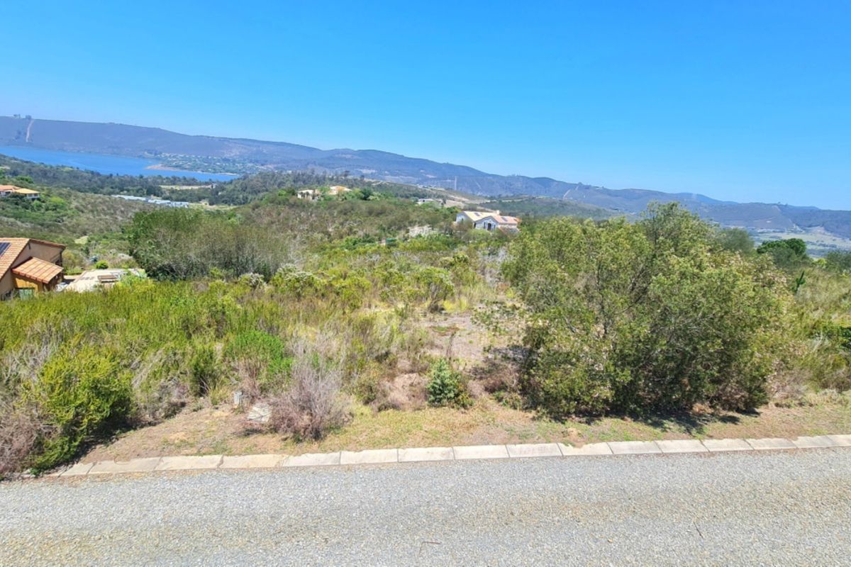A vacant residential plot featuring natural vegetation and expansive scenic views of the surrounding hills and distant water.