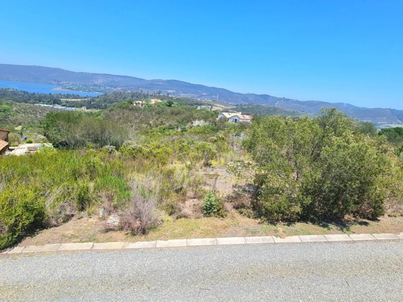 A vacant residential plot featuring natural vegetation and expansive scenic views of the surrounding hills and distant water.