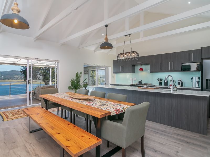 Spacious open-plan kitchen and dining area featuring vaulted ceilings with exposed rafters, modern cabinetry, and large sliding doors opening to a scenic balcony.