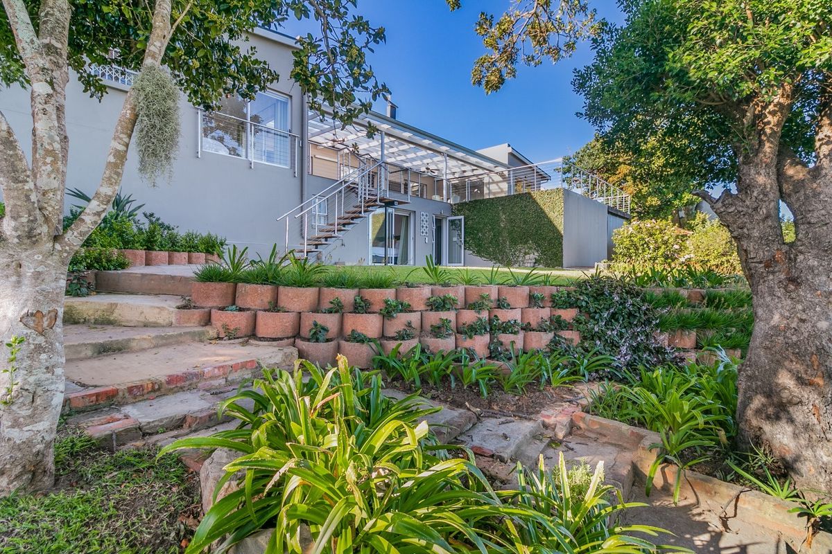 Rear view of the property featuring a multi-level landscaped garden, retaining walls, a raised balcony with a pergola, and an external staircase.