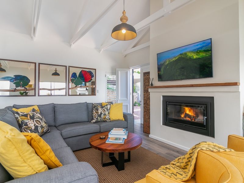 Cozy living room featuring a vaulted ceiling with exposed rafters, a modern built-in fireplace with a timber mantelpiece, and durable laminate flooring.
