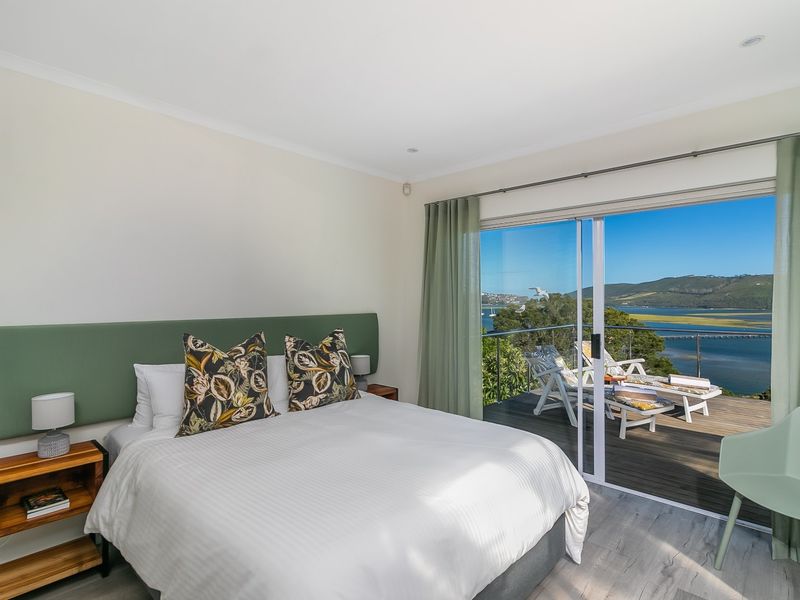 A bright bedroom featuring modern laminate flooring, recessed lighting, and a large sliding glass door opening onto a balcony with scenic water views.