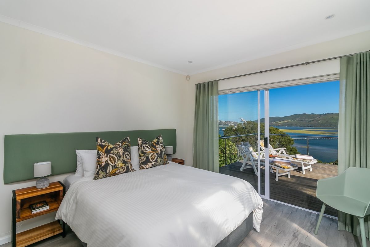 A bright bedroom featuring modern laminate flooring, recessed lighting, and a large sliding glass door opening onto a balcony with scenic water views.