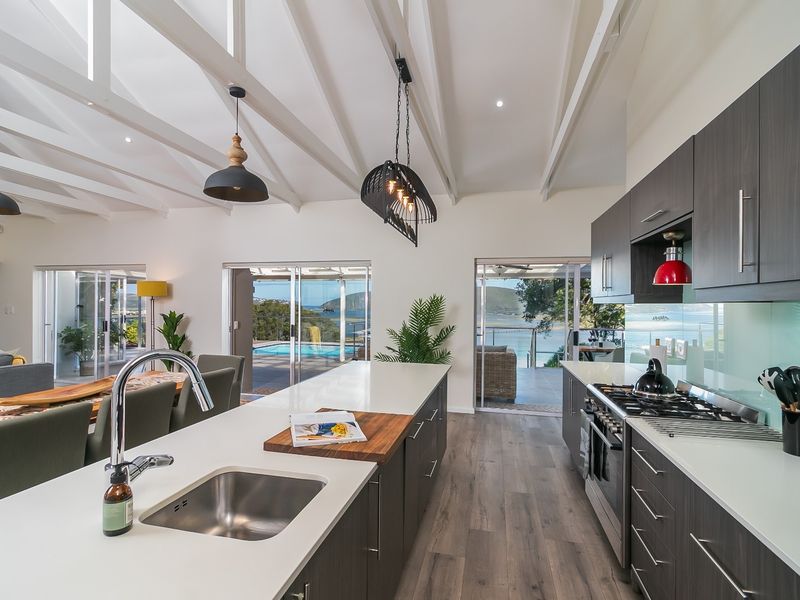 Modern open-plan kitchen and living area featuring a large island, gas cooktop, exposed vaulted ceilings, and seamless access to the outdoor patio and pool.