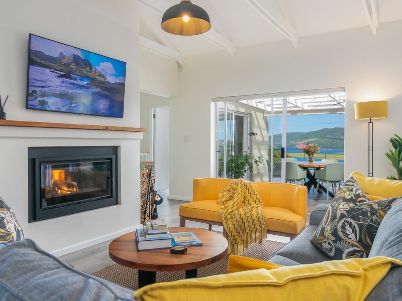 Bright living room featuring a built-in fireplace, vaulted ceilings, and sliding glass doors opening to a scenic patio with water views.