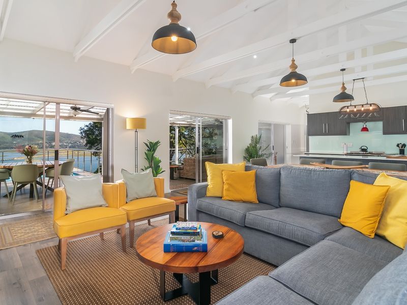 Spacious open-plan living and kitchen area featuring exposed white timber beams, modern cabinetry, and large sliding doors opening to a scenic outdoor patio.