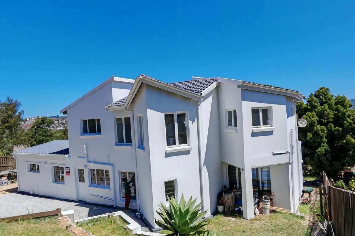 Rear view of a multi-story residential property featuring a tiled roof, paved patio area, and timber boundary fencing with ongoing exterior maintenance visible.
