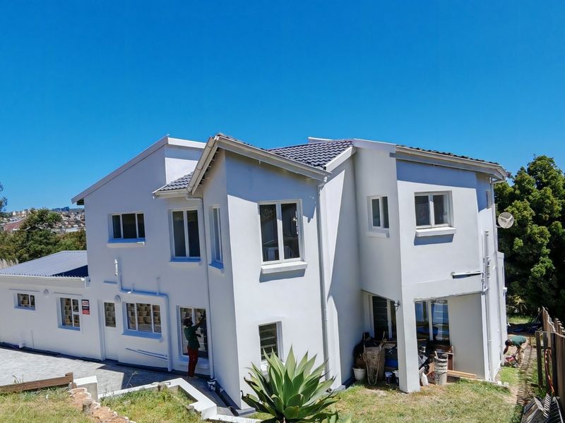 Rear view of a multi-story residential property featuring a tiled roof, paved patio area, and timber boundary fencing with ongoing exterior maintenance visible.