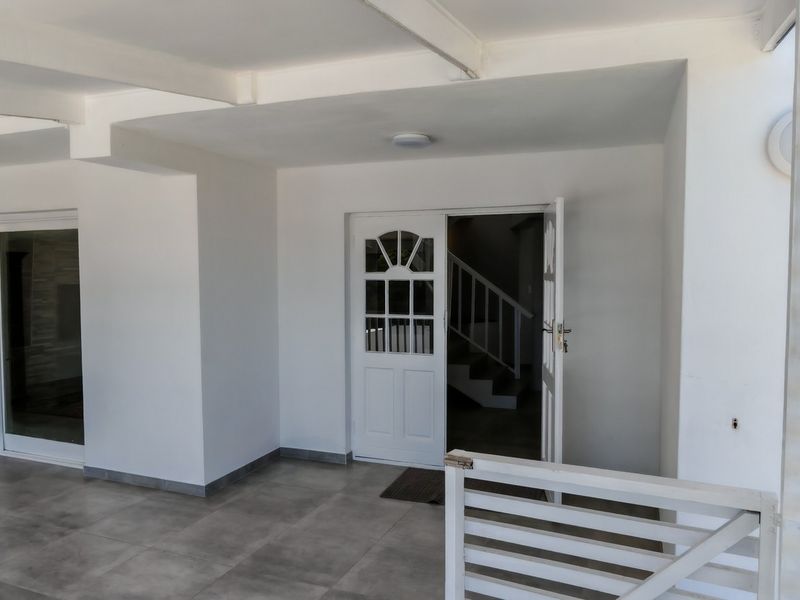 A spacious, covered patio area featuring modern tiled flooring, a built-in counter, and a timber privacy screen, providing a clean and versatile outdoor living space.