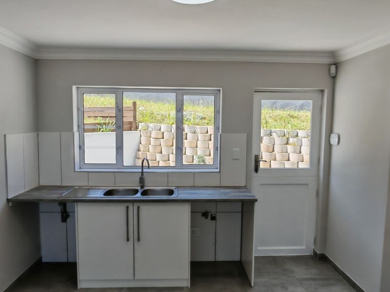 A clean, functional kitchen area featuring a double sink, laminate countertops, tiled backsplash, and direct access to the exterior through a side door.