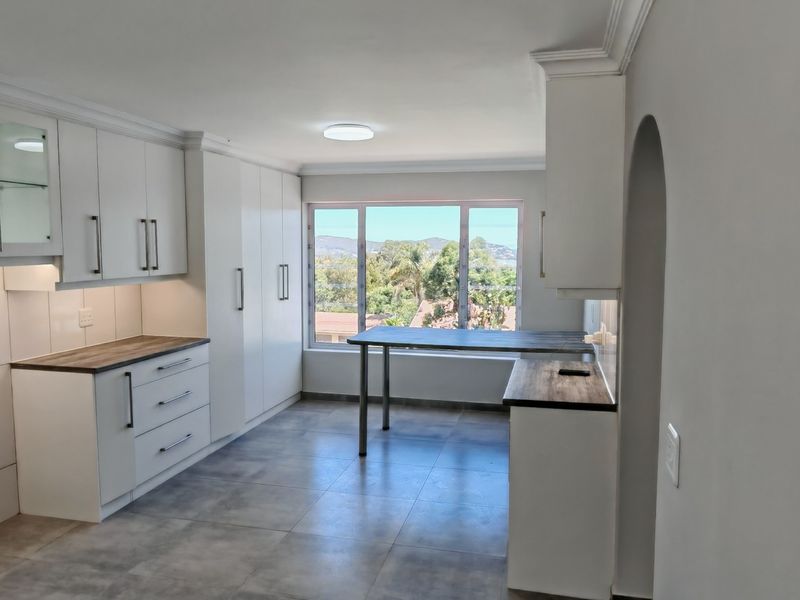 A modern, bright kitchen featuring white cabinetry, laminate countertops, tiled flooring, and a large window with scenic views.